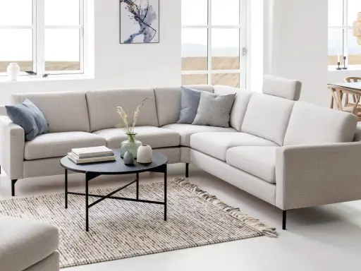 En ljus, modern hörntyp av soffa med kuddar och ett runt soffbord framför.
