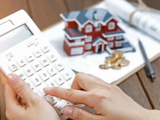 Calculando la casilla 435 renta: una mano usa una calculadora blanca junto a una maqueta de casa, monedas y planos.