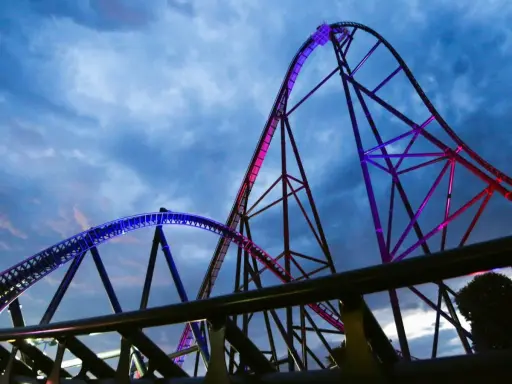 Najwyższy rollercoaster na świecie, oświetlony niebieskim i różowym światłem, wznosi się na tle burzowego nieba.