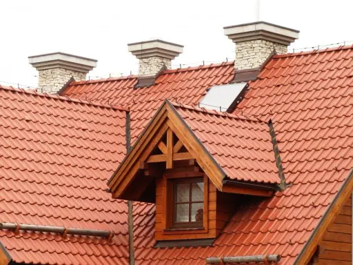 Dach dwuspadowy z czerwonej dachówki, z kominami i lukarną. Instalacja odgromowa zabezpiecza budynek.