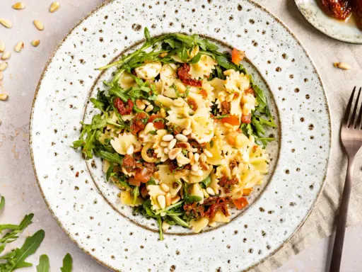 Ein köstlicher mediterraner Salat mit Farfalle, getrockneten Tomaten, Rucola und Pinienkernen.