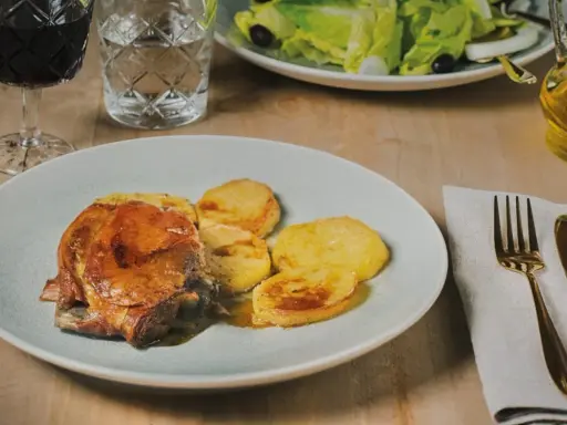Plato de carne asada con patatas, un ejemplo de comida típica de Huesca. Acompañado de ensalada, vino tinto y aceite de oliva.