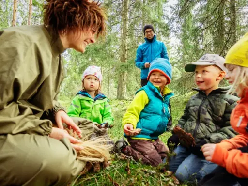 En grupp barn och en vuxen njuter av en dag i mulle skogen, omgivna av träd och grönskande natur.