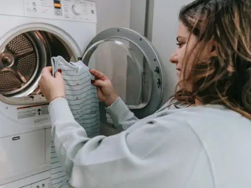 Mujer revisa una prenda antes de meterla a la secadora, pensando en como hacer que encoja la ropa.