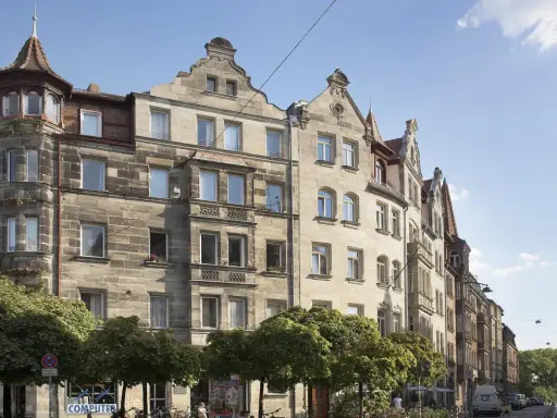 Ein prächtiges Jugendstil Haus mit Erker und Türmchen, umgeben von Bäumen, steht an einer belebten Straße.