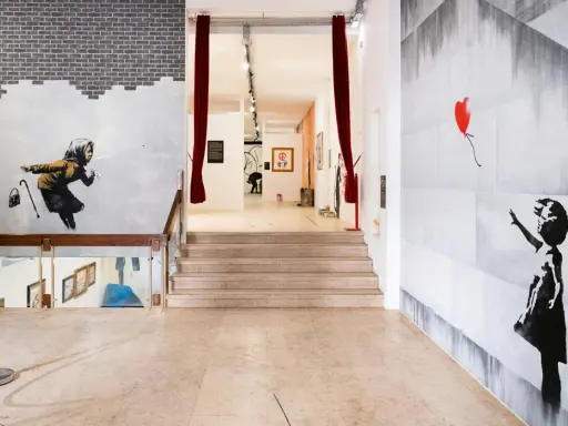 Banksy Lissabon: ikonische Werke wie das Mädchen mit dem roten Ballon und die wegspritzende Frau zieren die Wände einer Ausstellung.
