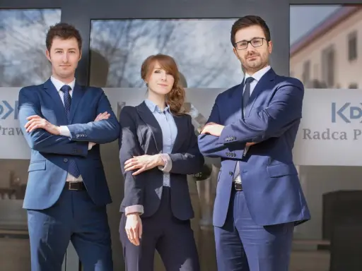 Trzech prawników w garniturach stoi przed budynkiem z logo "Radca Prawny".