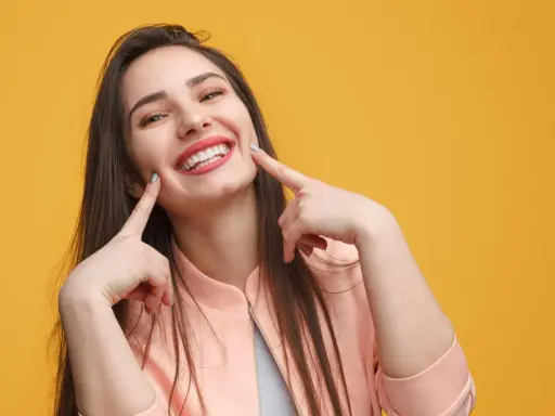 Une jeune femme au sourire éclatant, doigts pointés vers ses joues, semble expliquer la signification d'un sourire pincé.