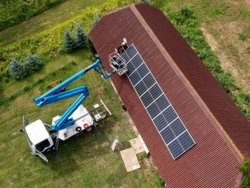 Installatörer monterar solpaneler på ett tak med hjälp av en kranbil. Solpaneler omvandlar solljus till likström (DC), som sedan kan omvandlas till växelström (AC) för användning i hemmet.