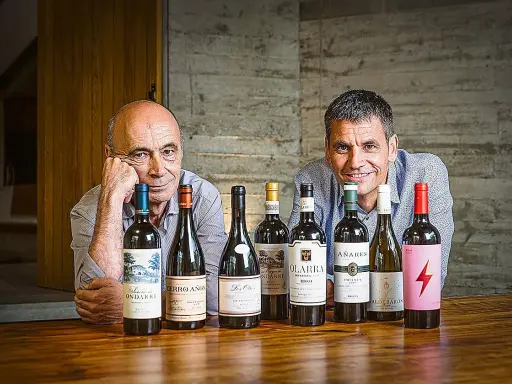 Dos hombres sonríen detrás de una fila de botellas de vino. Uno de ellos es el dueño de Bodegas Olarra.