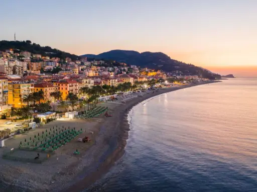 Alba sulla spiaggia finale ligure, con file di ombrelloni verdi e palme che si affacciano sul mare calmo.