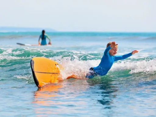 Niño sonriente surfeando en Portugal, una actividad genial que ver en Portugal con niños.