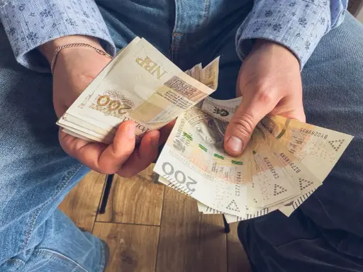 Ręce trzymające stos banknotów 200 zł. To może być wynagrodzenie urlopowe, które pozwoli na zasłużony odpoczynek.