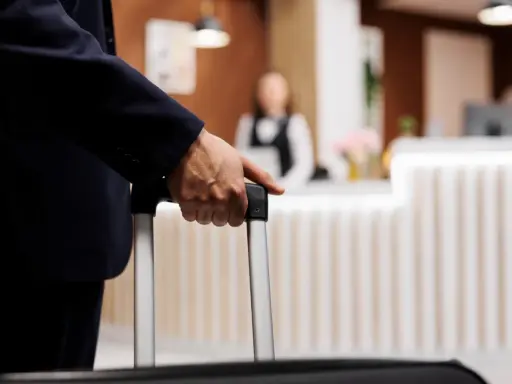 Mężczyzna w garniturze trzyma walizkę, zbliżając się do recepcji hotelowej. Czas na depozyt w hotelu i nowy początek podróży.