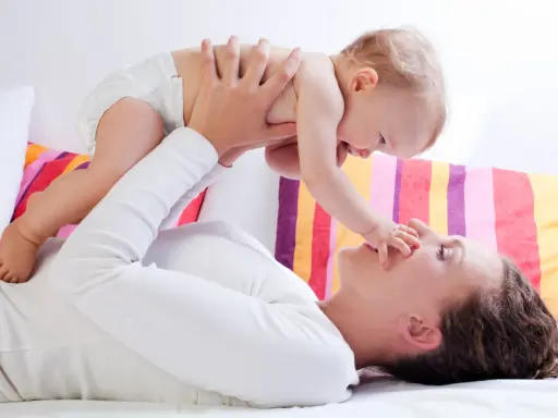 Mama podnosi dziecko, które wyciąga rączkę do jej nosa. Zdjęcie symbolizuje troskę o rozwój malucha, jak omega 3 dla niemowląt.