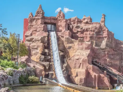 Aventura acuática en uno de los parques de atracciones en España. Un tronco desciende por una cascada artificial en un paisaje rocoso.