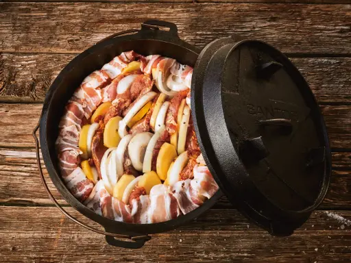 Dutch oven mit Fleisch, Kartoffeln und Zwiebeln, bereit für köstliche Dutch Oven Rezepte auf dem Gasgrill.