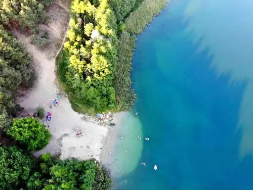 Plaża nad jeziorem tętni życiem. Ludzie odpoczywają na piasku, kąpią się w krystalicznie czystej wodzie, ciesząc się letnim dniem.