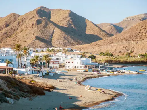Pueblos de Almería con playa, casas blancas y palmeras junto a un mar azul, con montañas áridas de fondo.