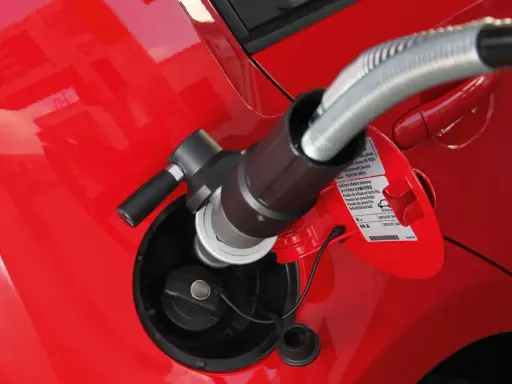 Tankowanie auta gazem CNG. Wlew paliwa w czerwonym samochodzie, do którego podłączona jest dysza.