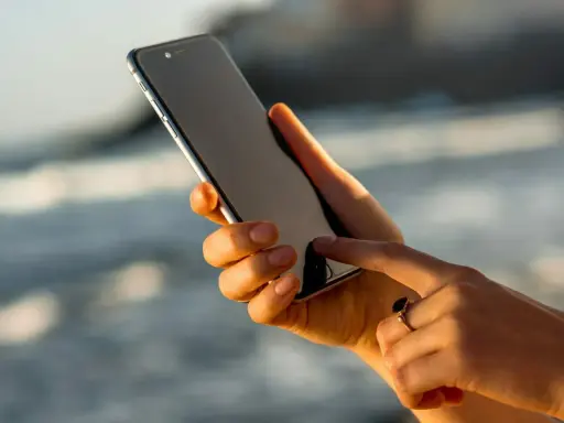 Dłoń trzyma iPhone 13, który nie chce się włączyć. Palec wskazujący próbuje go ożywić.