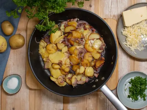 Bratkartoffeln rezept: goldbraune Kartoffeln mit Zwiebeln und Käse in der Pfanne, dazu frische Petersilie und Salz.