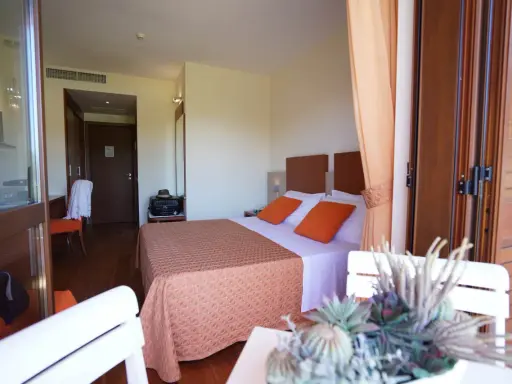 Camera accogliente al Valtur Otium Resort, con letto comodo, cuscini arancioni e vista sulla porta scorrevole in legno.