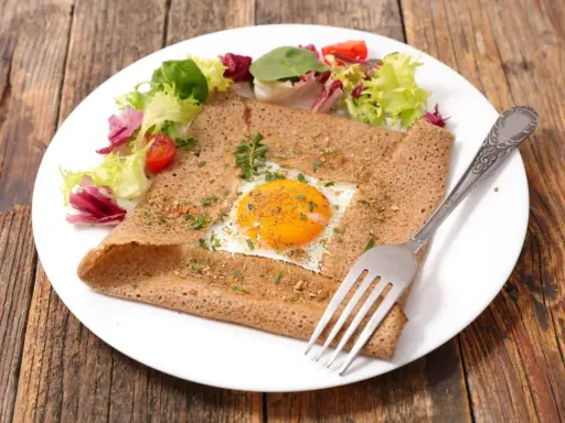 Galette bretonne complète au four, garnie d'un œuf au plat, d'herbes et servie avec une salade fraîche.