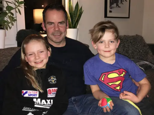 Marcus Oscarsson med sin familj, dottern och sonen sitter glatt i soffan.