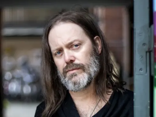 Niclas Frisk med långt hår och skägg, blickar mot kameran.