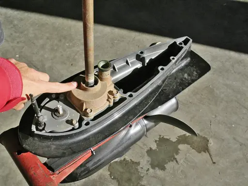 Main d'une personne en veste rouge pointant vers la turbine d'un moteur hors-bord Yamaha 2 temps, prêt à changer la pièce.