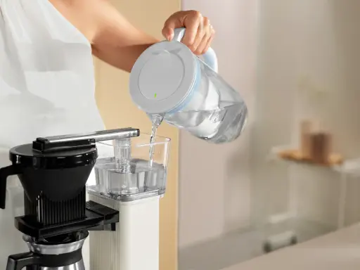 Eine Person füllt Wasser in eine Filterkaffeemaschine, um sie zu entkalken.