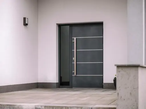 Nowoczesne drzwi wejściowe, ciemnoszare, z długą, metalową klamką i bocznym przeszkleniem. Czy to drzwi stalowe czy aluminiowe?