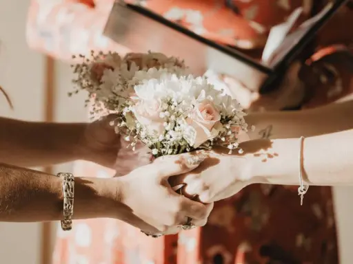 Manos entrelazadas sosteniendo un ramo de flores, un momento íntimo de los rituales boda civil.