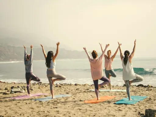 Kvinnor i trädposition på stranden. En lugn morgon för yoga, kanske en paus från pilates.