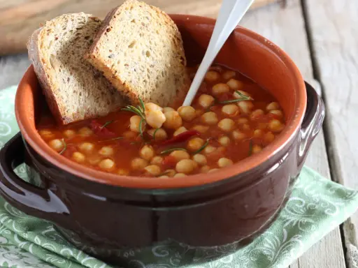 Una ciotola di terracotta con zuppa di ceci, pomodoro e rosmarino, accompagnata da fette di pane rustico.