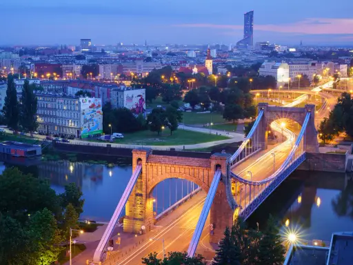 Most Wrocławia w niebieskiej godzinie. Most Grunwaldzki i ruch uliczny tworzą świetlne smugi na tle miasta.