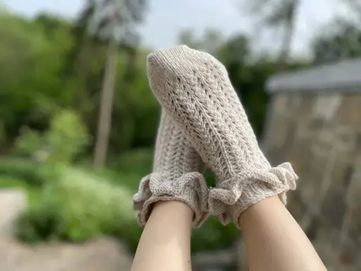 Piernas con calcetines de crochet color crema, con volantes en los tobillos y un delicado patrón calado.