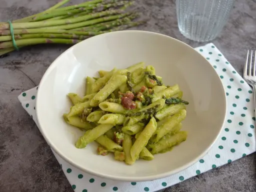 Penne cremose con asparagi freschi e cubetti di speck croccante, un piatto primaverile gustoso.