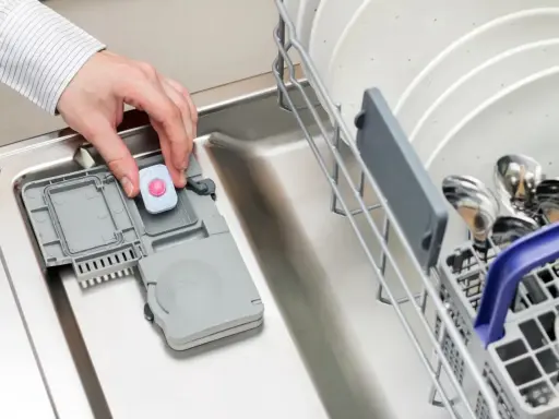 Dłoń wkłada tabletkę do zmywarki. Może to być rozwiązanie problemu, gdy zmywarka nie domywa górnego kosza.