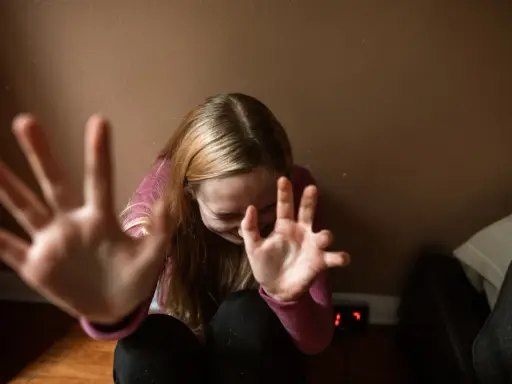 Dziewczyna z rozczochranymi włosami, z rękami przed twarzą, jakby broniła się przed nadmierną kontrolą.