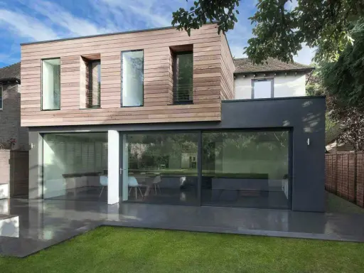 Une extension moderne en bois et anthracite pour agrandir une maison, avec de grandes baies vitrées donnant sur un jardin.