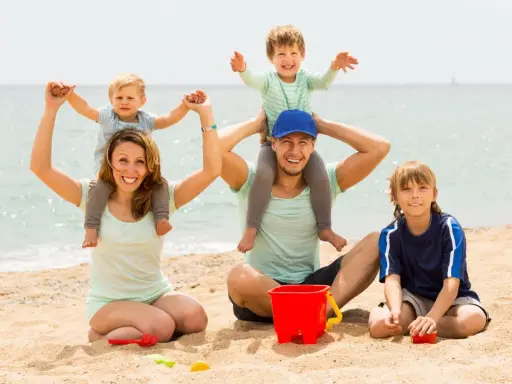 Famiglia felice in spiaggia, un modo perfetto per imparare come abbronzarsi in sicurezza mentre i bambini giocano con secchiello e palette.