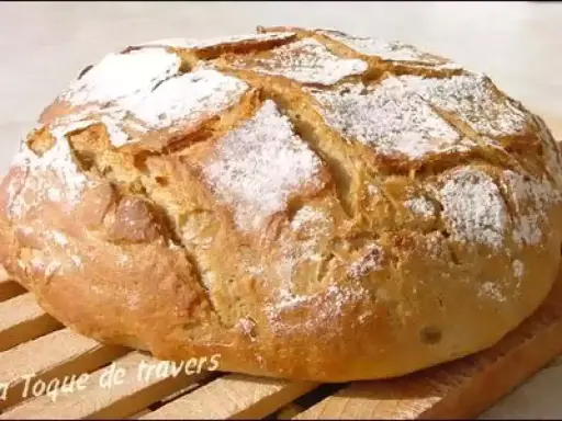 Gros pain artisanal, saupoudré de farine, avec une croûte dorée et des incisions. Ce pain farine de chataigne semble tout juste sorti du four.
