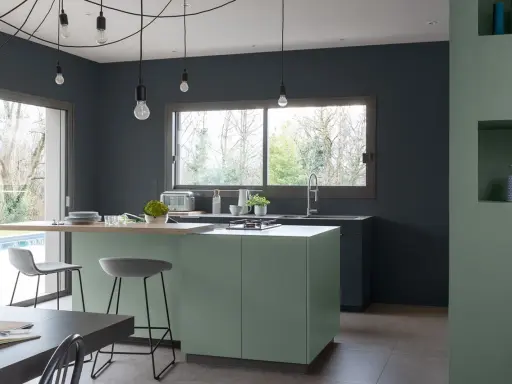 Cuisine moderne aux murs gris anthracite. L'îlot central vert sauge et le plan de travail en bois clair invitent à la convivialité. Quelle peinture pour plafond ? Un blanc mat pour agrandir l'espace.
