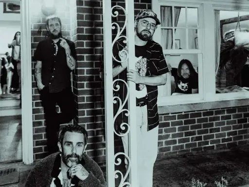 Band of Horses i Stockholm. Fyra män poserar utanför ett hus, en tittar ut genom ett fönster.