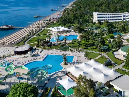 Widok z lotu ptaka na Mirage Park Resort: plaża, baseny, zjeżdżalnie wodne, białe pawilony i hotele otoczone zielenią.