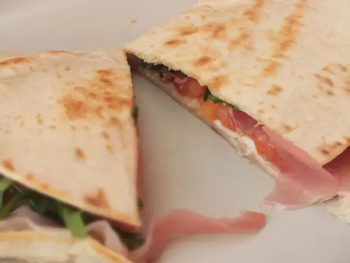 Pyszna piadina z szynką, pomidorami i rukolą, złożona na pół, prezentuje apetyczny przekrój.