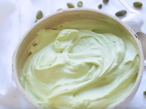 Un bol rempli de ganache pistache onctueuse, parsemé de pistaches entières. Une gourmandise verte et appétissante.