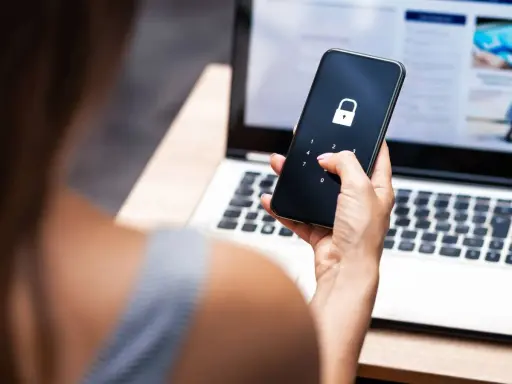 Frau entsperrt Handy mit Schloss-Symbol, besorgt wegen gehackter mailadresse. Laptop im Hintergrund.